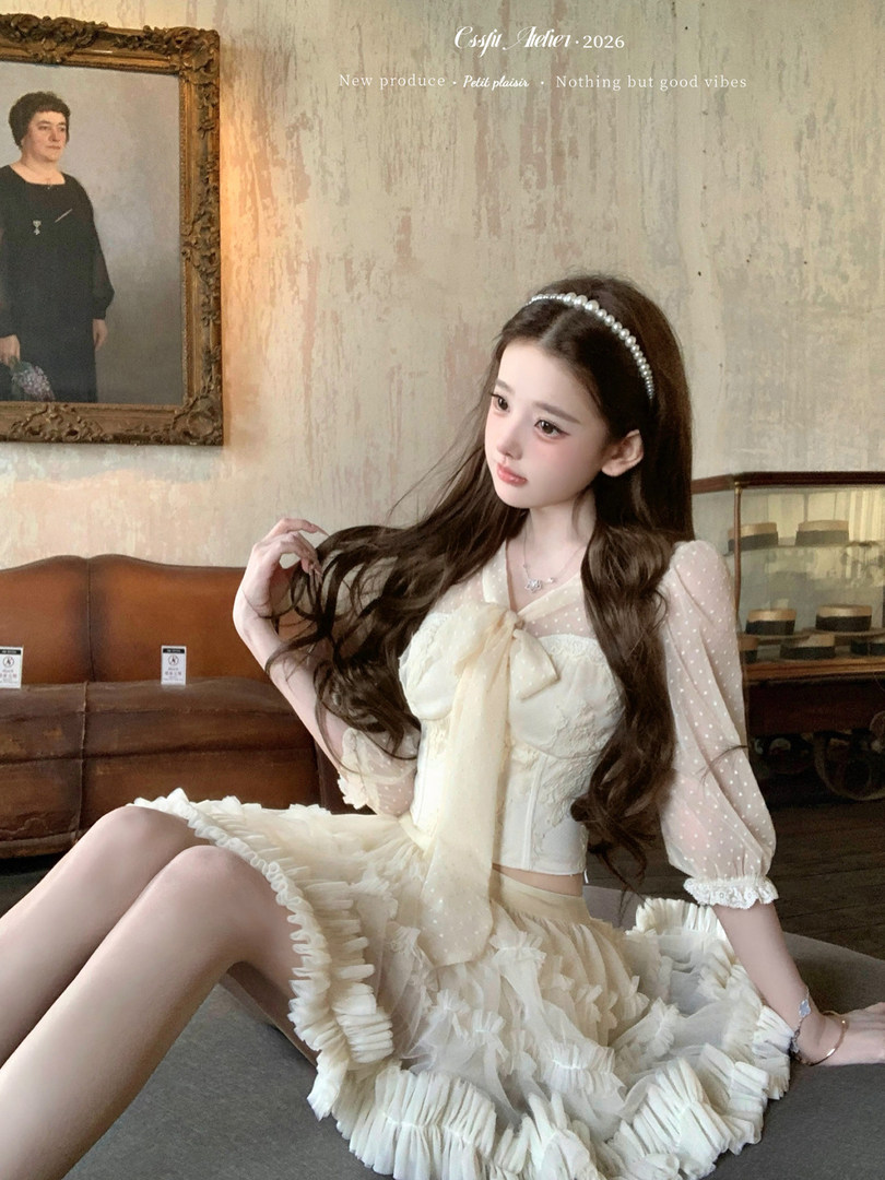 Model wearing a cream ruffled lace dress with sheer sleeves and a pearl headband