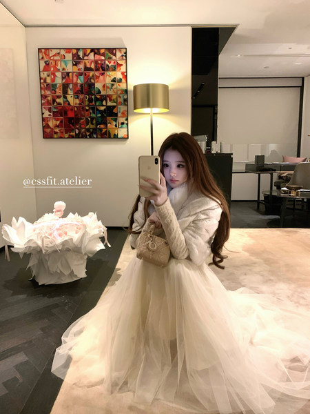 Woman wearing a cream tulle formal dress with a fur shawl and small beige handbag