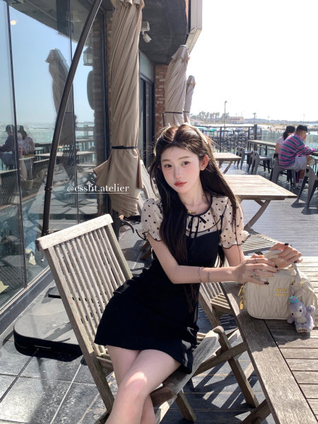 Woman wearing a black mini dress with sheer polka-dot sleeves at a seaside cafe