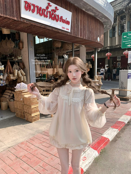 Model wearing a cream sheer lace-trimmed blouse outdoors