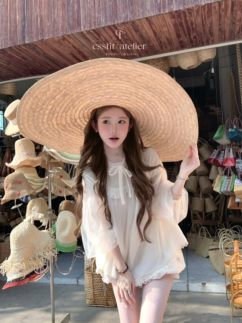 Model wearing a sheer white outfit with a large straw hat at a hat shop