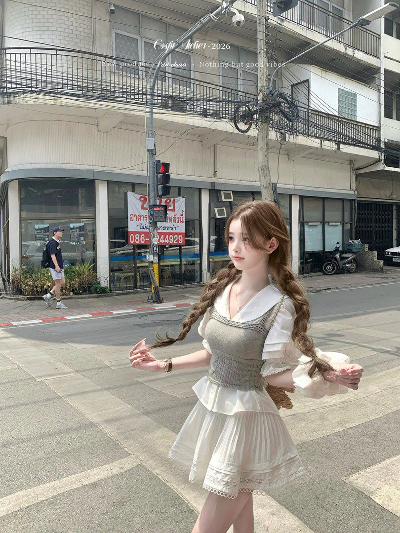 Woman wearing a white blouse with a gray layered dress and pleated skirt outdoors