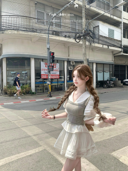 Woman wearing a white blouse with a gray layered dress and pleated skirt outdoors