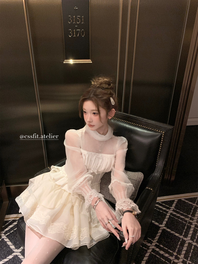 Model wearing a white sheer lace dress seated on a chair