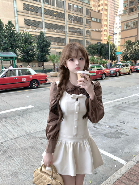 Young woman wearing a cream pinafore dress with a brown blouse on a city street
