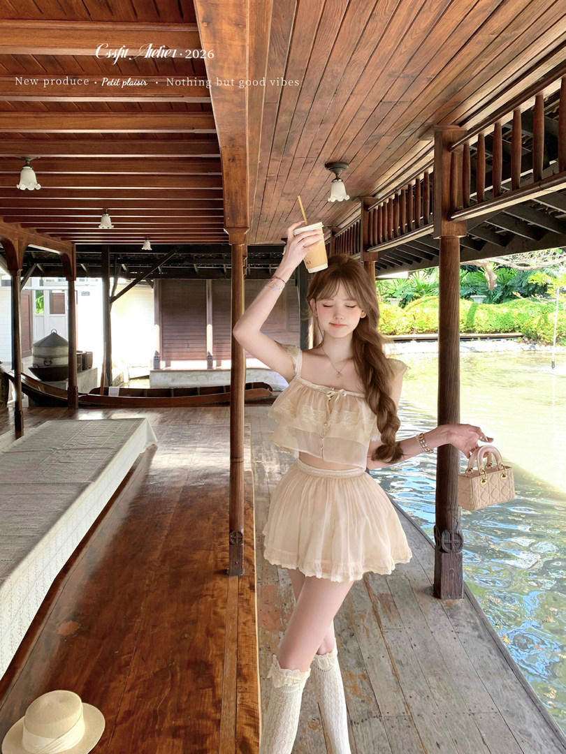 Model wearing a cream two-piece ruffled outfit with lace knee-high boots by the water