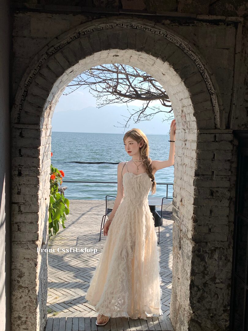 Woman wearing a light beige lace maxi dress by the seaside archway