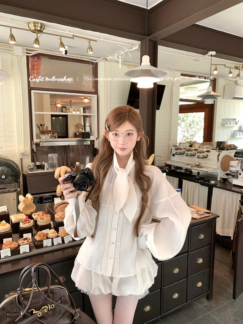 Young woman wearing a white sheer blouse and matching ruffled shorts in a cafe