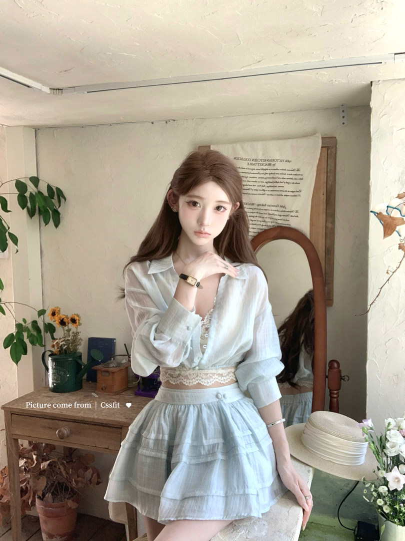 Model wearing a white sheer blouse and light blue layered skirt