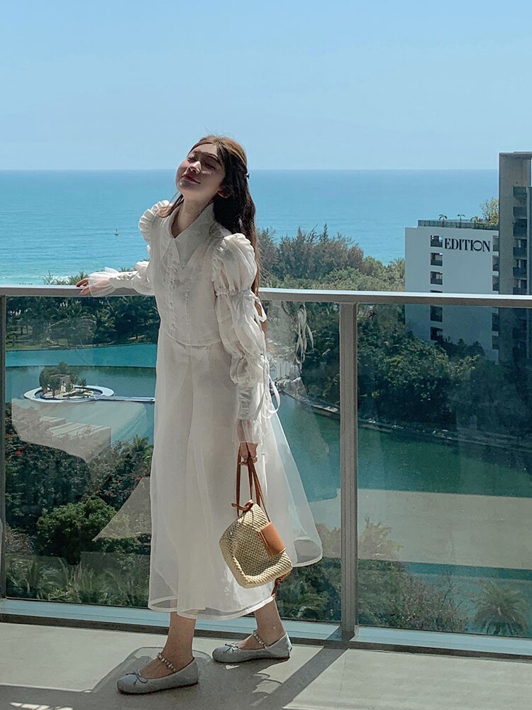 Woman wearing a white long dress and holding a woven handbag by the seaside