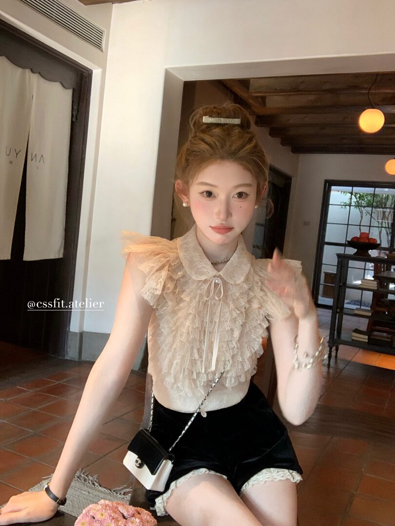 Model wearing a cream lace ruffled sleeveless top with black shorts