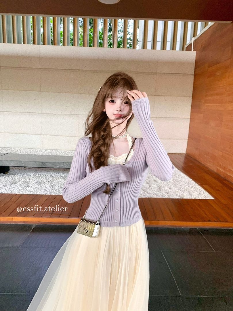 Model wearing a lavender ribbed cardigan with a cream pleated skirt and small chain handbag