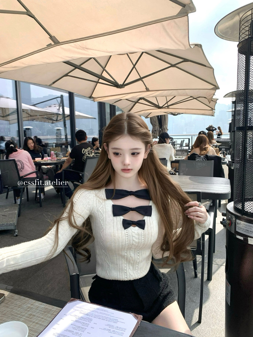 Woman wearing a cream knit top with black bow details at an outdoor café.