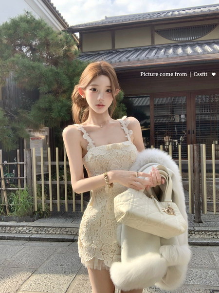 Woman wearing a cream lace dress and holding a matching handbag outdoors.