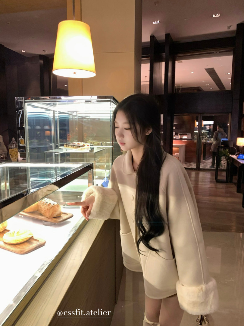 Beige winter coat with faux fur cuffs worn by a model in a café