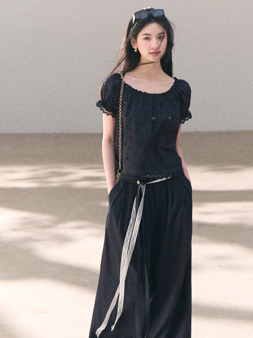 Model wearing a black off-shoulder top with wide-leg pants and a chain-strap bag