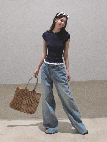 Model wearing a navy sleeveless top with light blue wide-leg jeans and holding a woven tote bag