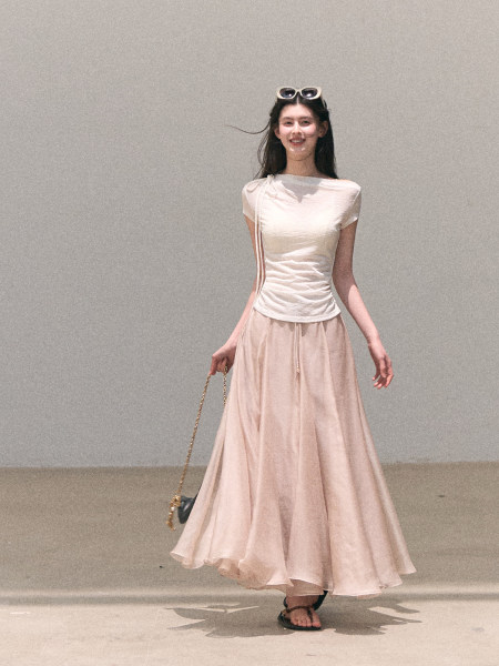 Model wearing a cream fitted top with a blush flowing maxi skirt and small handbag