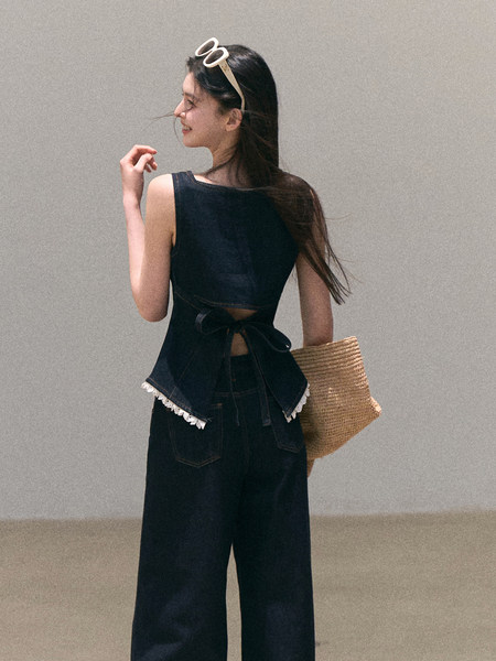 Model wearing a dark sleeveless top and wide-leg pants with a woven straw bag
