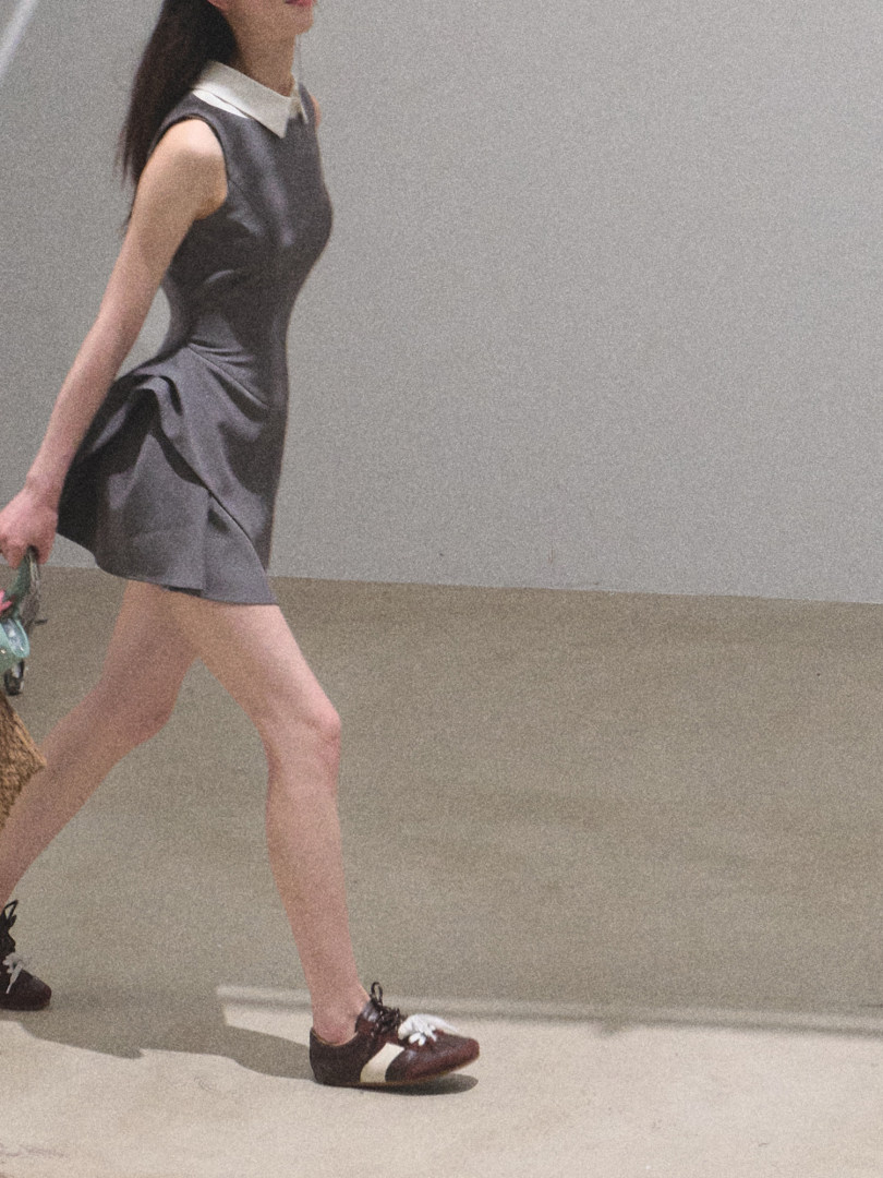 Model wearing a gray sleeveless dress with a white collar and brown sneakers