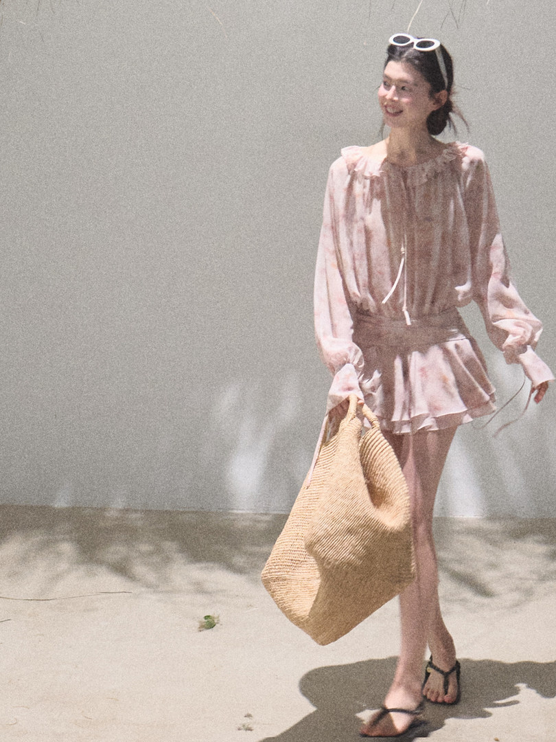 Woman wearing a light pink flowy outfit and carrying a large woven tote bag