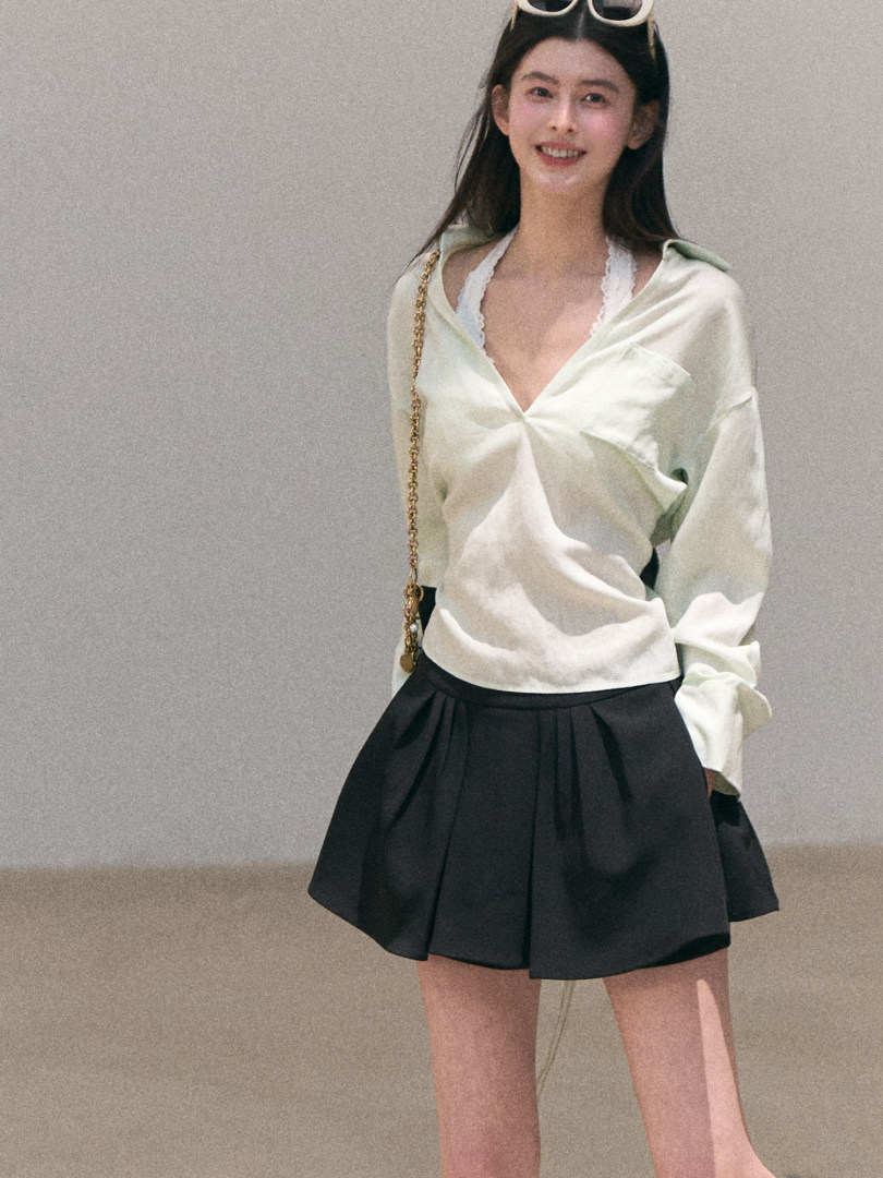 Model wearing a light satin wrap top with a black pleated mini skirt