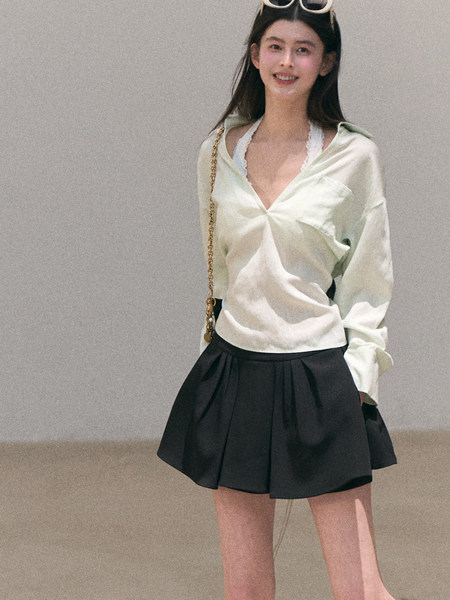 Model wearing a light satin wrap top with a black pleated mini skirt