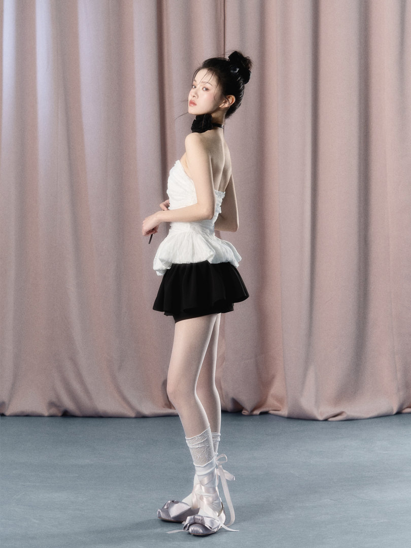 Model wearing a white strapless top with a black mini skirt and ballet-style shoes