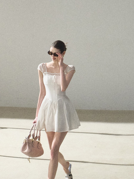 White sleeveless mini dress worn by a model with a handbag
