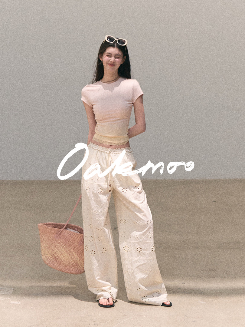 Model wearing cream eyelet wide-leg pants with a fitted pale top and straw tote