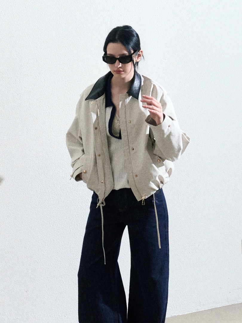 Model wearing a light beige jacket with black collar and wide-leg dark pants