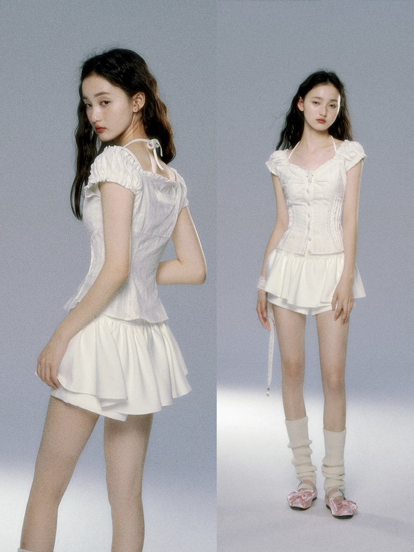 White feminine two-piece outfit worn by a model, featuring a ruched top and layered mini skirt