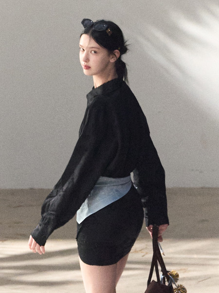 Model wearing a black long-sleeve top with a black mini skirt and layered shirt detail