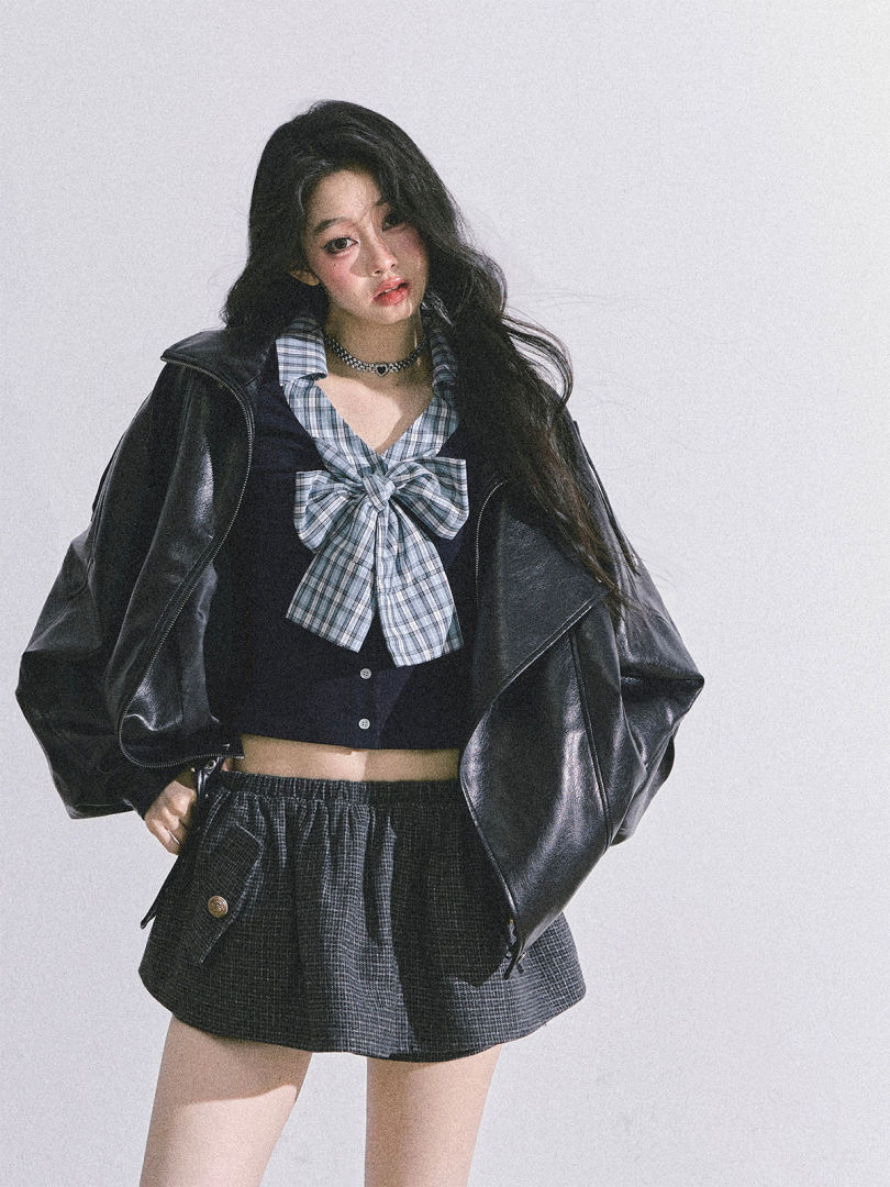 Model wearing a black leather jacket with a plaid bow top and gray mini skirt