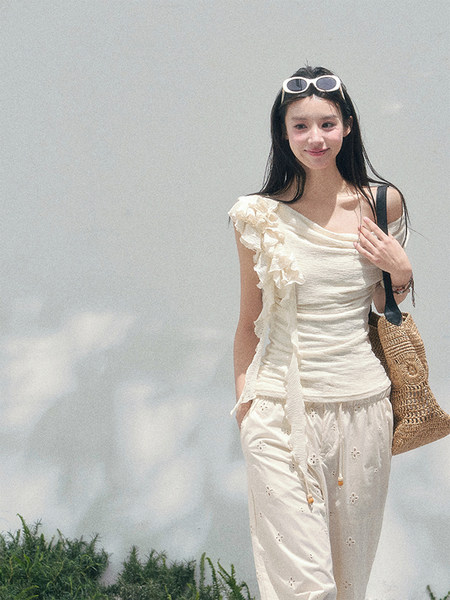 Woman wearing a cream ruffled top and matching white pants with a woven tote bag