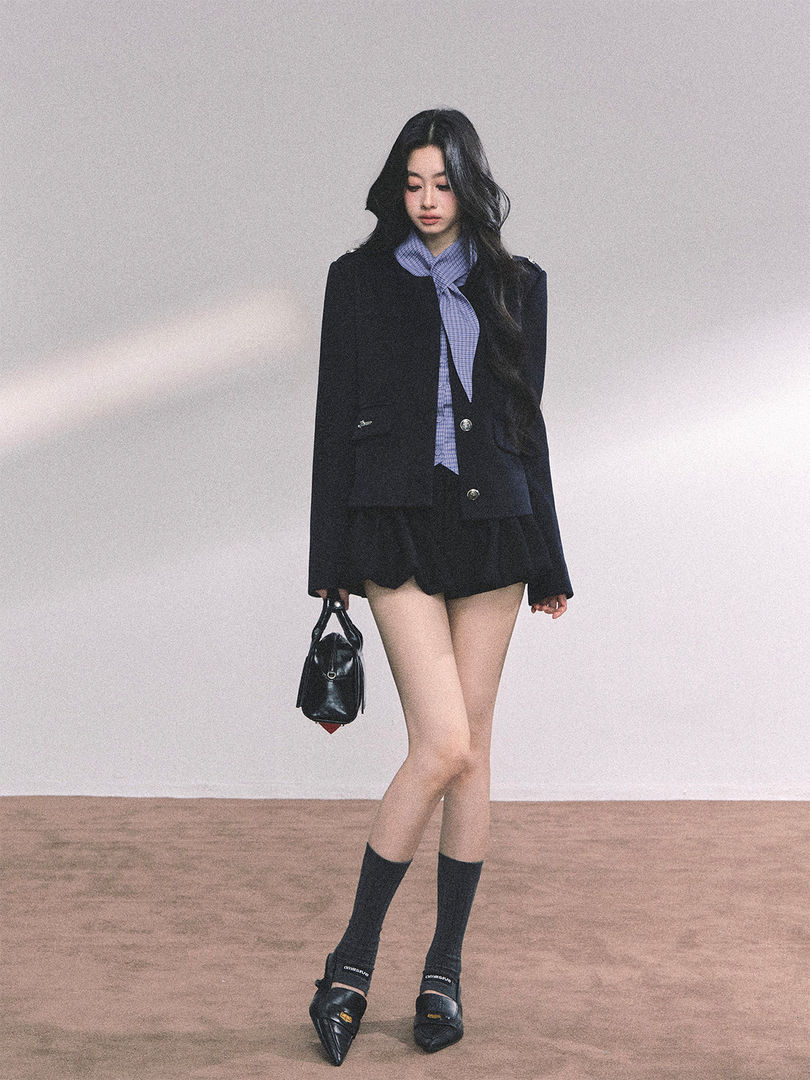 Fashion model wearing a black blazer outfit with a blue scarf and holding a black handbag