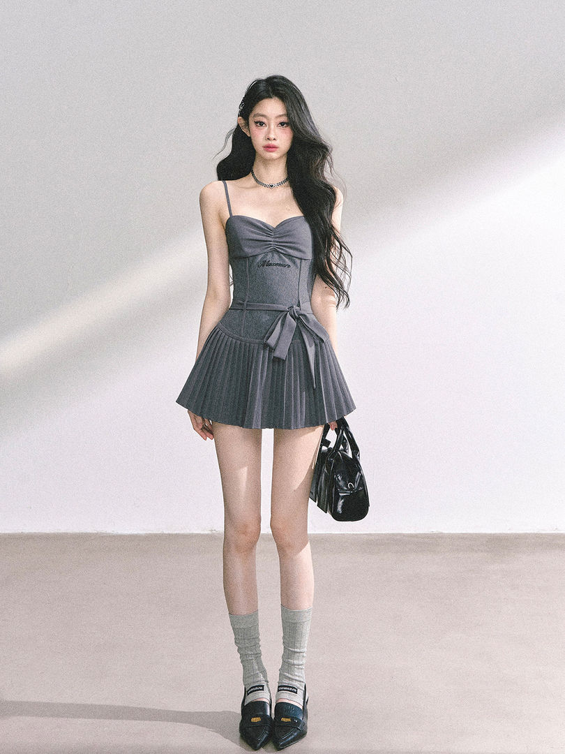 Model wearing a gray sleeveless pleated mini dress with a bow detail and handbag