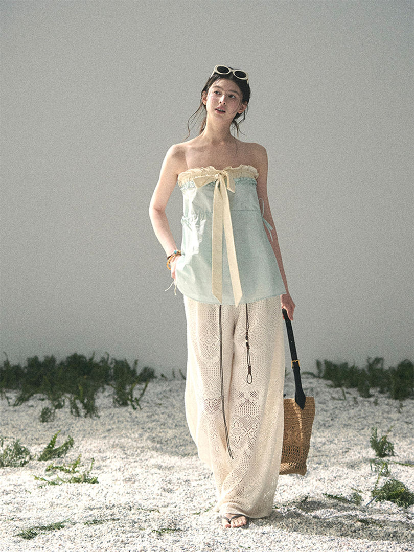 Model wearing a light blue strapless top with white lace pants on a beach