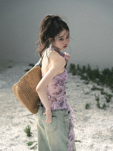 Woman wearing a purple halter top and light jeans with a woven straw tote bag