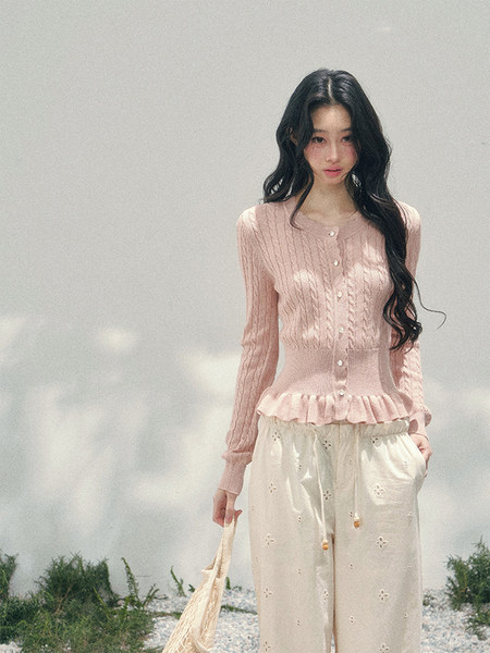 Model wearing a pink knit cardigan with cream eyelet pants