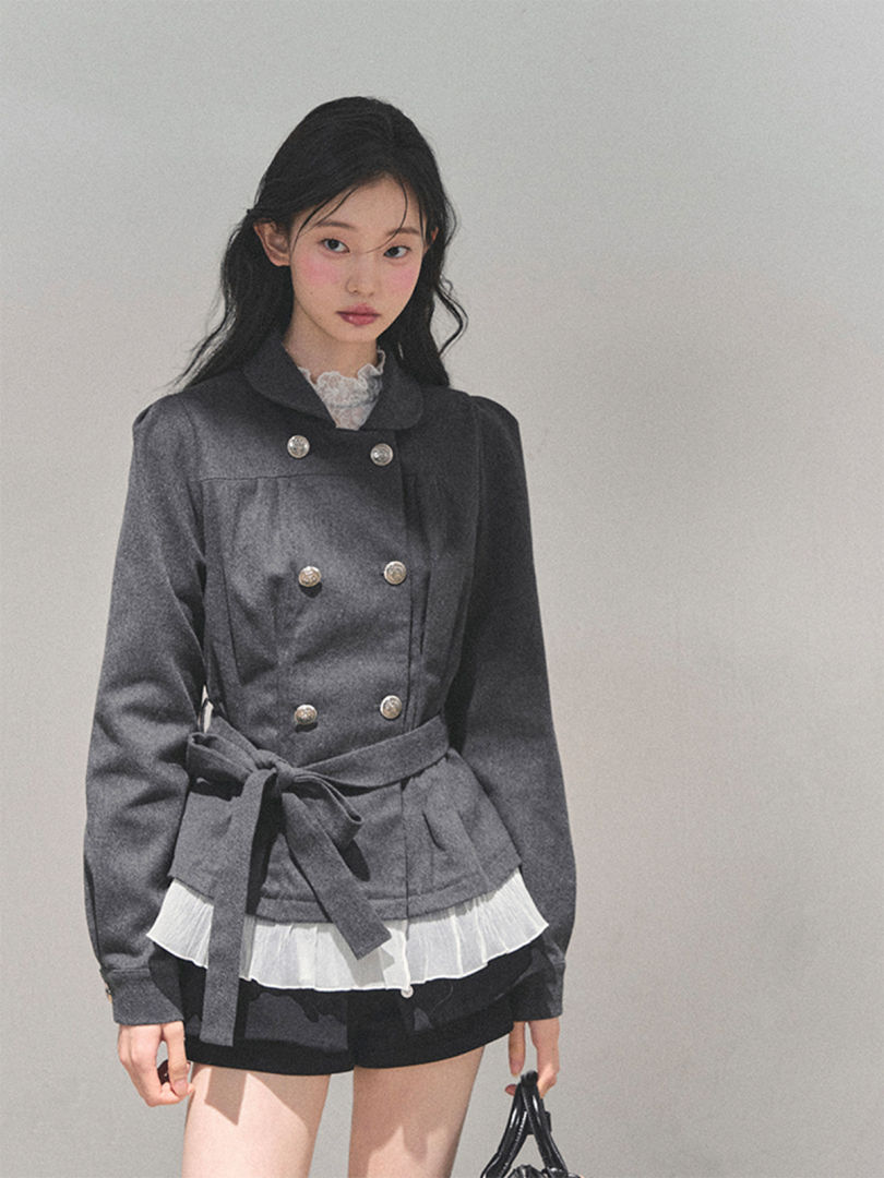 Model wearing a gray double-breasted belted jacket with black shorts and layered white hem