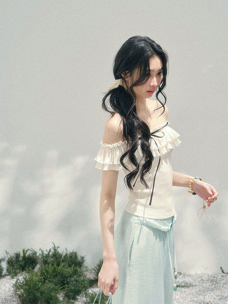 Model wearing a cream off-shoulder ruffled top with a light blue skirt