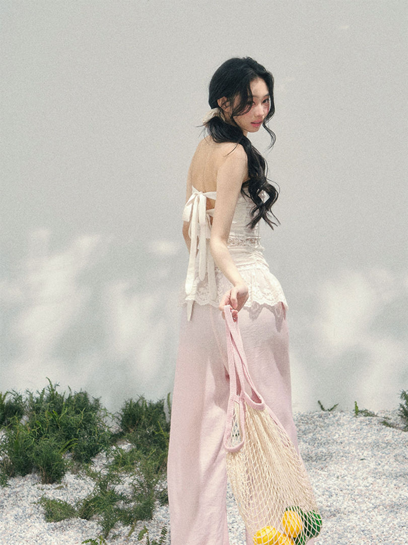 Woman wearing a white lace back-tie top with a pink maxi skirt on a beach setting