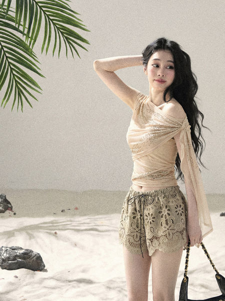 Model wearing a light beige off-shoulder top with lace shorts in a beach setting