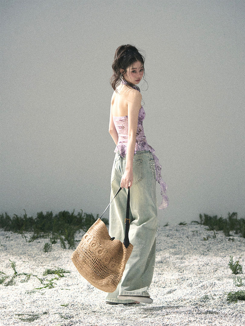 Model wearing a lavender strapless top with loose light-wash jeans and a woven straw tote bag outdoors