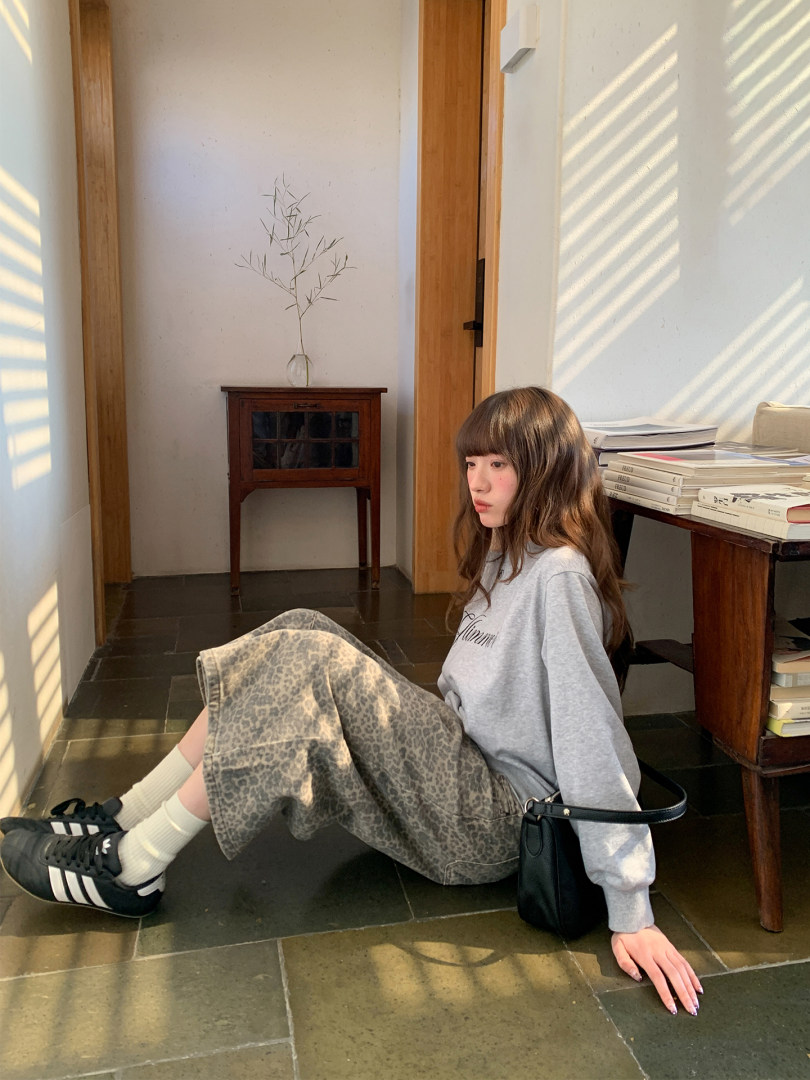 Woman wearing a gray sweatshirt, patterned skirt, black sneakers, and a small black shoulder bag