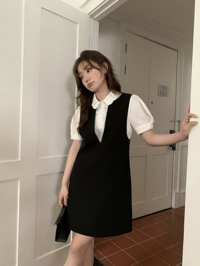 Model wearing a black sleeveless dress layered over a white puff-sleeve blouse
