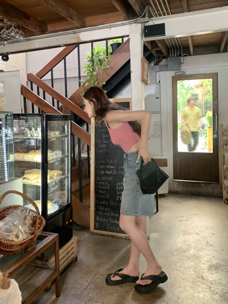 Woman wearing a pink crop top, denim skirt, and black sandals indoors