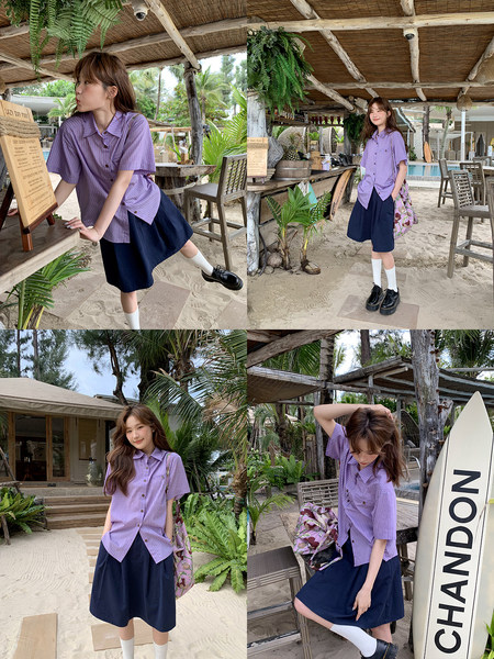 Model wearing a lilac striped short-sleeve shirt with a navy skirt in a tropical beach setting