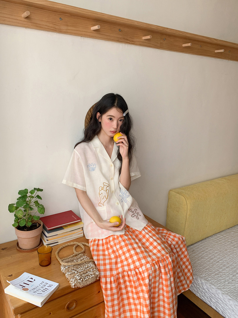 Model wearing a white embroidered short-sleeve top with an orange gingham skirt